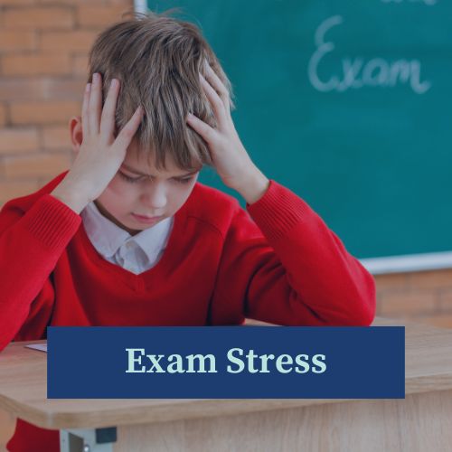 Young boy in school uniform sitting at a desk about to take an exam, with his head in his hands, looking anxious